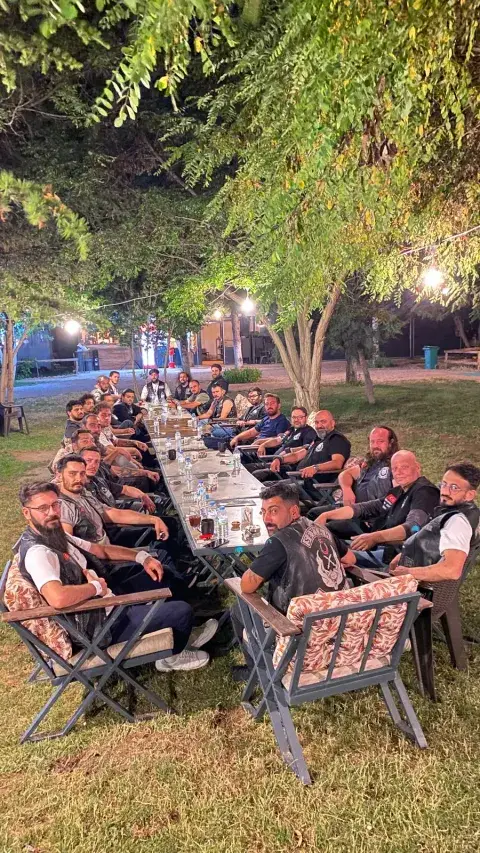 Ağaçlar altında uzun masada akşam yemeği yiyen grup, Konya