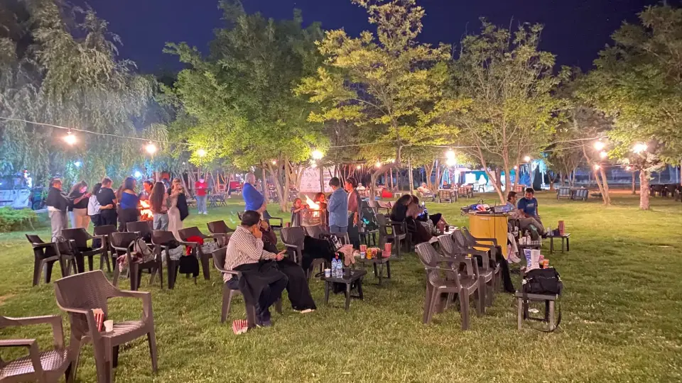 Ağaçlı çimlikte sandalyelere oturmuş izleyiciler, gece sineması Konya